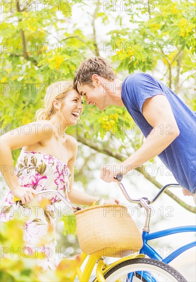 Portrait of young couple sitting on bicycles, touching foreheads, laughing