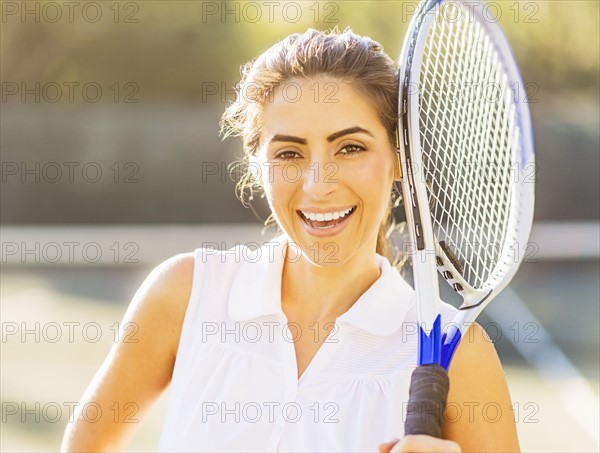 Portrait of smiling young woman holding tennis racket