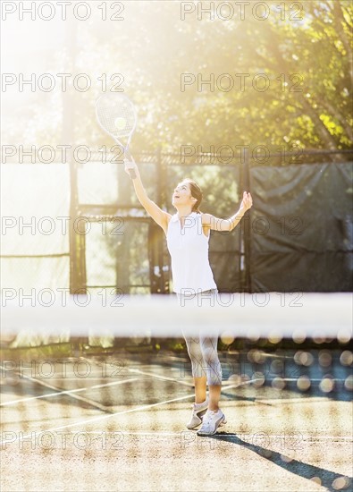 Young woman in tennis court about to serve ball with net in blurred foreground
