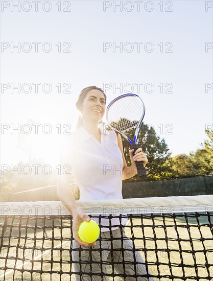 Portrait of young woman standing by net, holding tennis ball and tennis racket