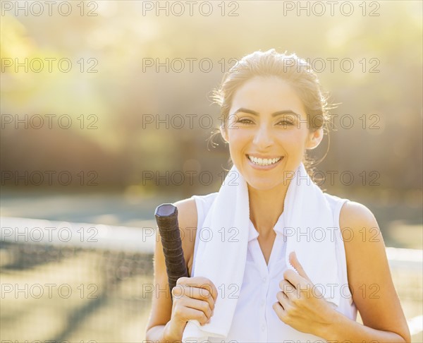 Portrait of smiling young woman with towel and tennis racket