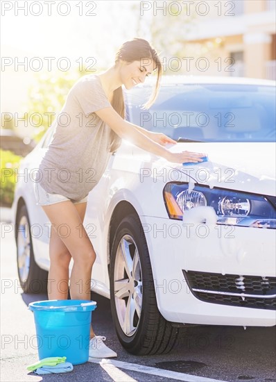 Portrait of young woman washing white car