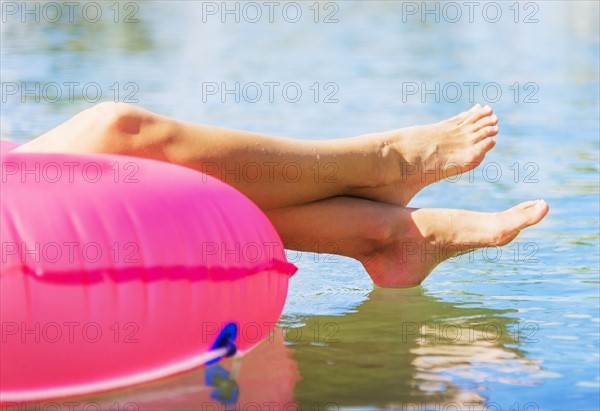 Cropped shot of legs of young woman floating on pink swim ring