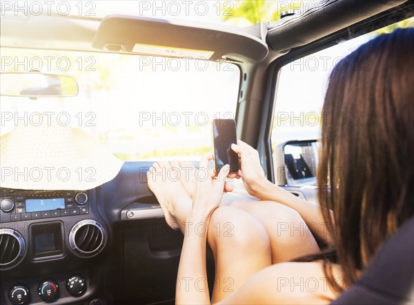 Young woman sitting in car with legs on dashboard using smart phone