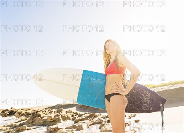 Portrait of young woman standing on beach, holding surfboard