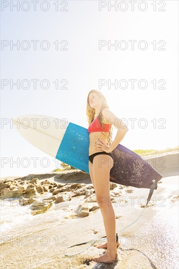 Portrait of young woman standing on beach, holding surfboard