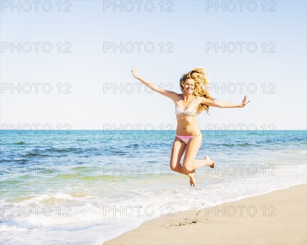 Portrait of young woman wearing bikini jumping on beach