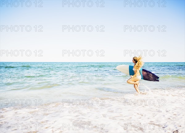 Young woman running in surf into sea carrying surfboard