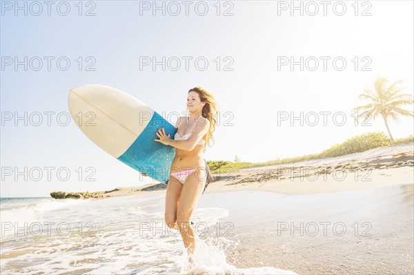 Young woman running in surf into sea carrying surfboard