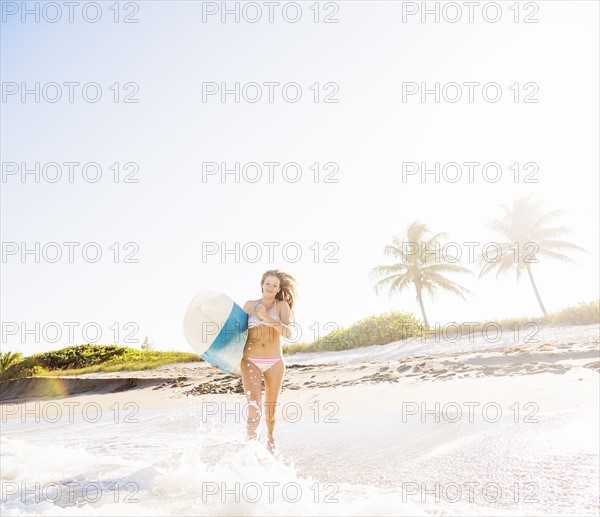 Young woman running in surf carrying surfboard