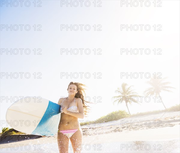 Young woman running in surf carrying surfboard