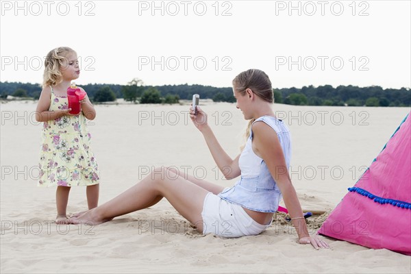 Mother taking picture of daughter (2-3) on beach