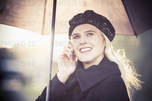 Smiling woman under umbrella using mobile phone