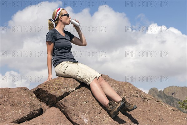 Woman sitting on rock and drinking from bottle