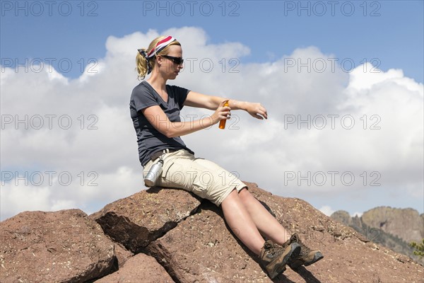 Woman sitting on rock and applying suntan lotion