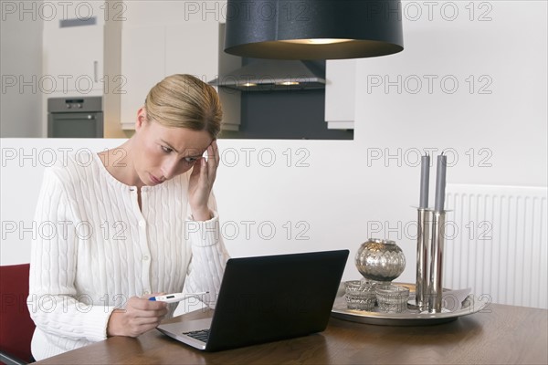 Overworked woman using laptop and holding thermometer