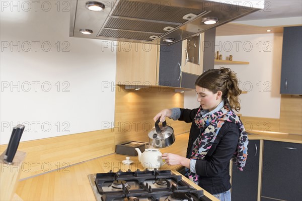 Woman pouring water at teapot in kitchen