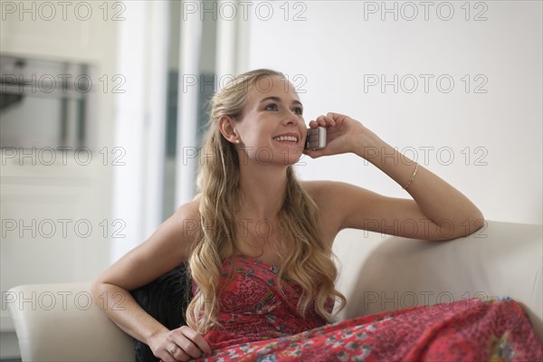 Woman in dress sitting on sofa and using phone