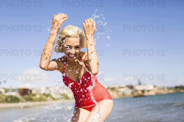 Woman in red swimming costume splashing water on beach