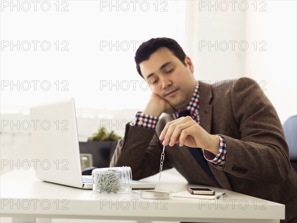 Businessman sitting in office and playing with paper clips