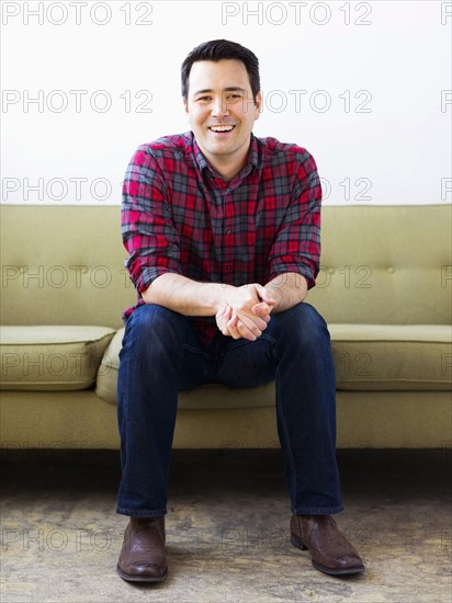 Man in checked shirt sitting on sofa and posing to camera