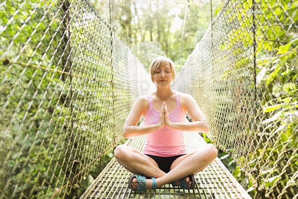 Woman practicing yoga on footbridge in forest