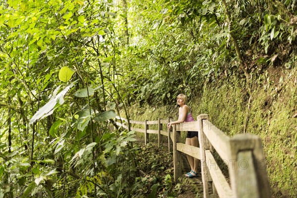 Woman in forest leaning against wooden fence