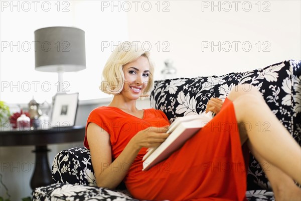 Woman in red dress lying down on sofa and holding book
