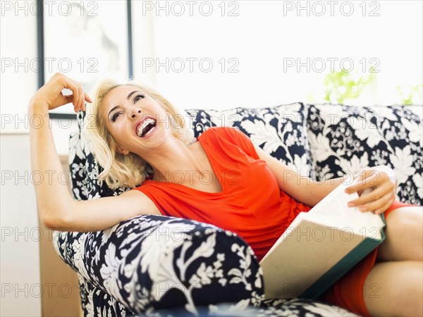 Woman on sofa holding book and laughing