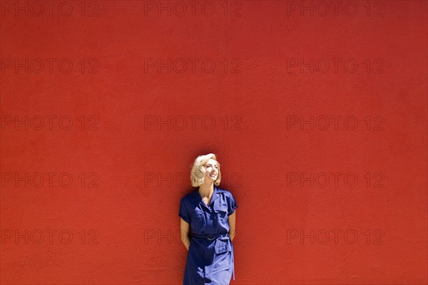 Woman in blue dress posing against red wall in sunlight