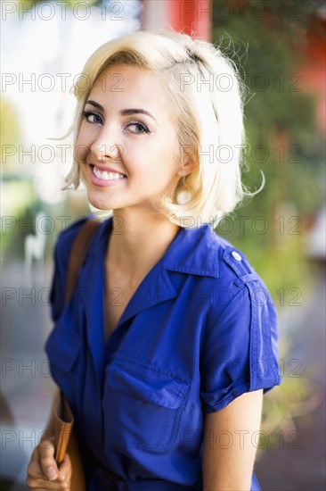 Woman with dyed hair and wearing blue dress looking at camera