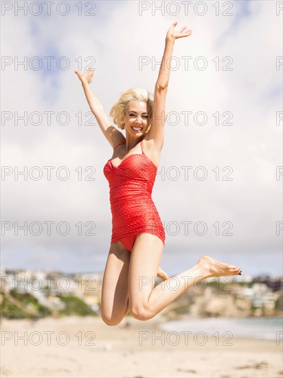 Woman wearing red one piece swimsuit jumping on sandy beach