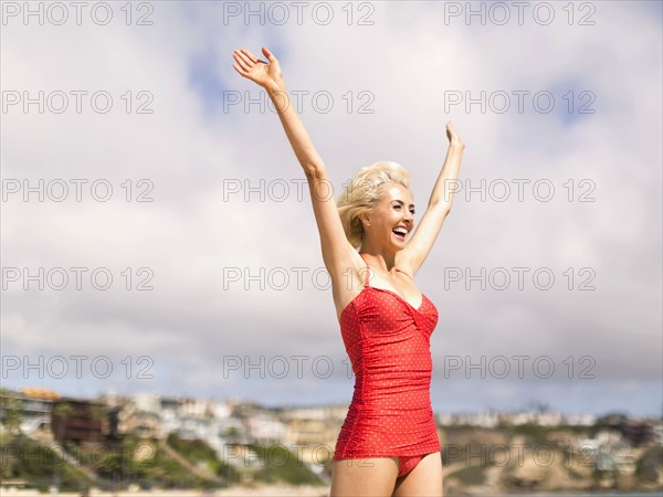 Woman wearing red one piece swimsuit standing on beach with arms raised