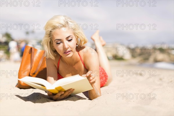 Portrait of blond woman reading book on beach