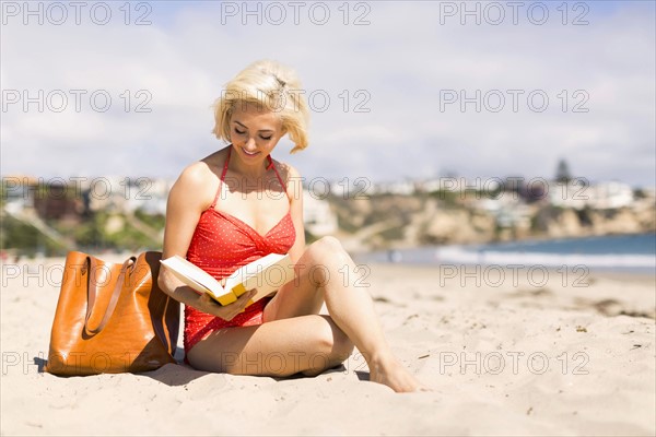 Portrait of blond woman reading book on beach