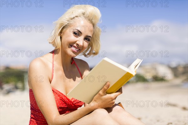 Portrait of blond woman reading book on beach