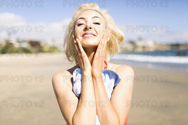 Portrait of blond woman on beach applying sun screen
