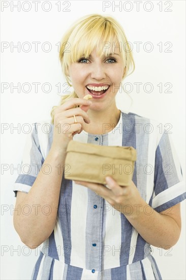Studio shot of woman eating cashews from paper bag
