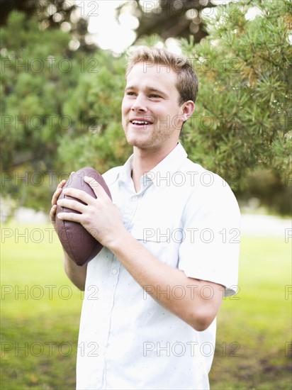 Portrait of young man holding football in park