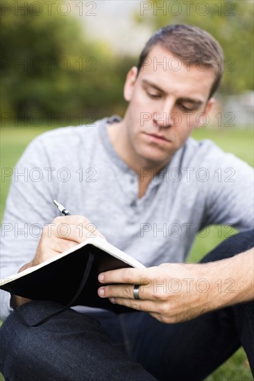 Portrait of young man writing journal in park