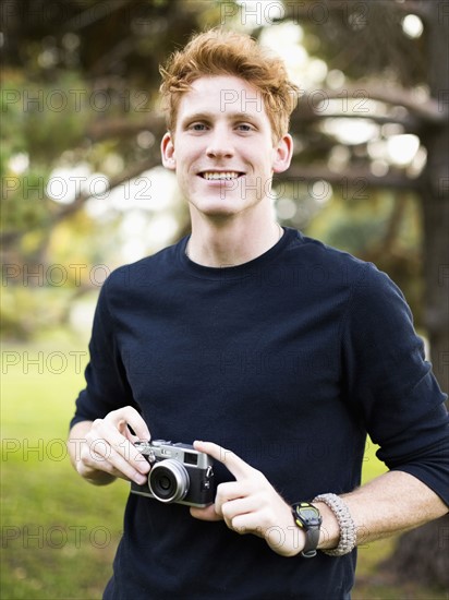 Portrait of young man holding camera in park