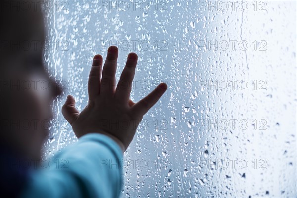 Close-up of girl's hand on wet window.