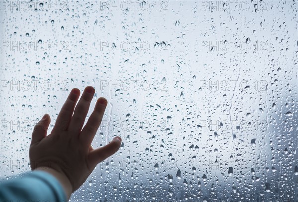 Close-up of girl's hand on wet window.