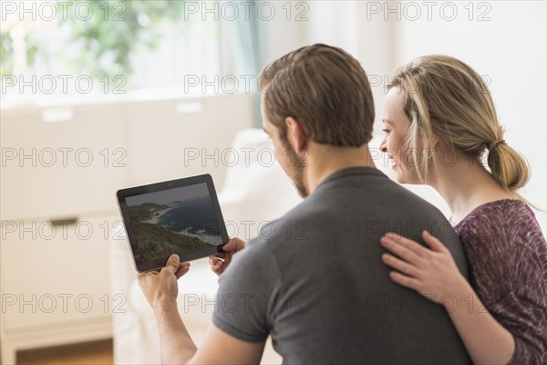 Rear view of couple looking at picture on digital tablet.