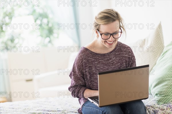 Young woman sitting on bed and using laptop.