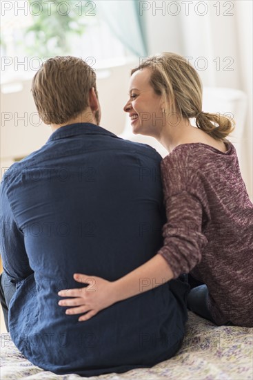 Rear view of young couple sitting on bed.