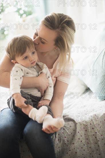 Mother kissing little son (2-3 years) on bed.