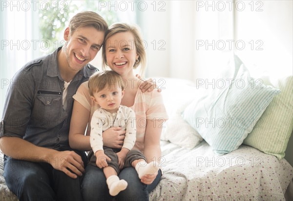 Happy parents with little son (2-3 years) sitting on bed.