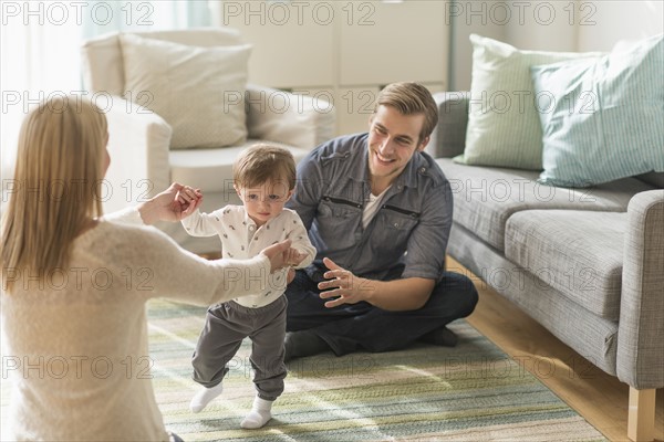 Happy parents helping little son (2-3 years) walking in living room.