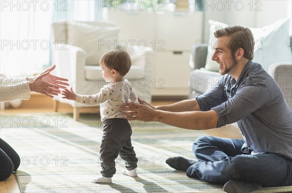 Happy parents helping little son (2-3 years) walking in living room.